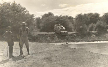 my father in his Landrover about to cross a river watched by 2 local tribesmen